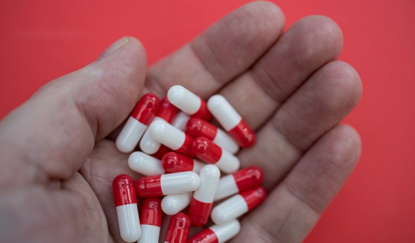 Red and white tianeptine antidepressant pills, which are unregulated by the FDA, on a hand on a red background